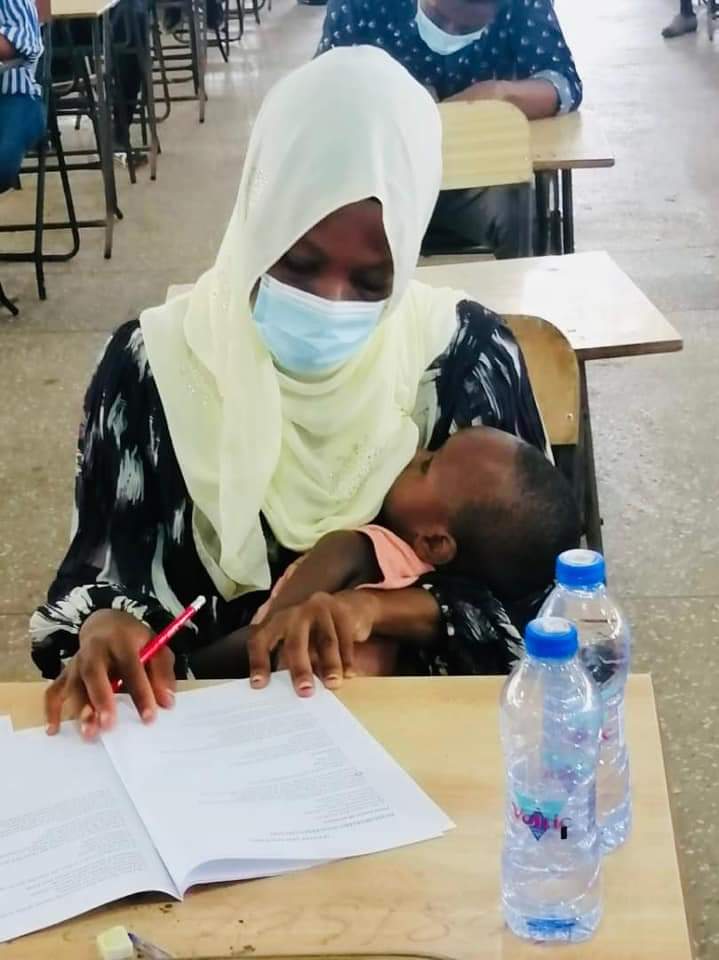 A determined young Ghanaian breast feeding mother writes exams with her baby .